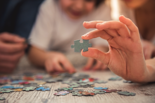 Person holding up jigsaw puzzle piece while working on a puzzle